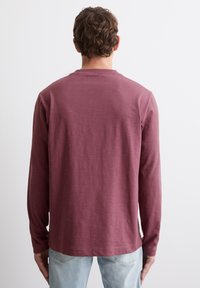 Langarmshirt in gedämpftem Burgunderrot, aus weichem Stoff gefertigt. Verfügt über einen Rundhalsausschnitt und einen nahtlosen Rücken, mit einer lockeren Passform.