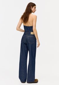 Denim strapless top paired with wide-leg jeans in dark blue. Features a leather patch on the back and decorative studs along the pockets.