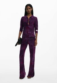 Blouse à motifs floraux violets avec col et manches longues, assortie à un pantalon évasé, fabriquée dans un tissu lisse et texturé.
