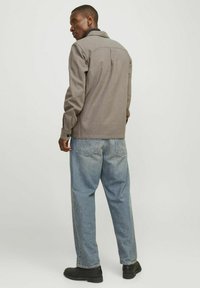 Giacca grigia a maniche lunghe con colletto, polsini con bottoni e dettaglio della spalla sul retro, abbinate a jeans larghi di colore blu chiaro e scarpe nere.