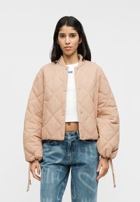 Ανοιχτόροζ καπιτονέ μπουφάν τύπου bomber με στρογγυλή γιακά, κουμπιά με πάτημα και ελαστικές μανσέτες, φορεμένο πάνω από λευκό τοπ και μπλε τζιν.