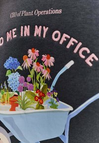 Grafická tričko s modrým vozíkom naplneným farebnými kvetmi – ružovými sedmikráskami, modrými hortenziami a fialovými fialkami – na tmavom pozadí.