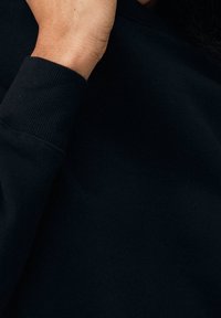 Gros plan d'une main ajustant le col d'une chemise ou d'un pull noir à manches longues.