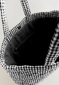 Black and white checkered fabric tote bag with quilted texture, two handles, and black inner lining with a zippered pocket.