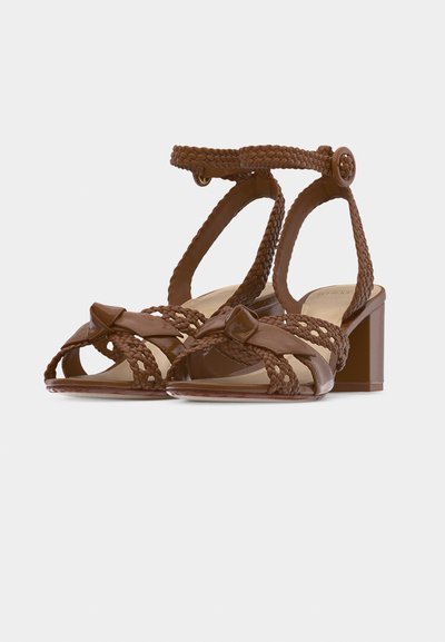 Καφέ δερμάτινα σανδάλια με πλεκτούς ιμάντες, τετράγωνες φτέρνες και κλείσιμο με αγκράφα στον αστράγαλο, σχεδιασμένα για τη γυναικεία μόδα.