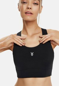 Schwarze Sport-BH mit glatter Textur, breiten Trägern und rundem Ausschnitt. Mit kleinem weißen Logo in der Mitte.