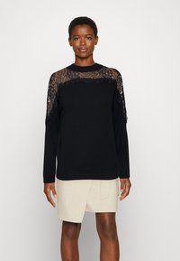 Schwarzes Langarmshirt mit Spitzenpaneelen an den Schultern und im oberen Rückenbereich. Glatte Textur mit Rundhalsausschnitt und normaler Passform.