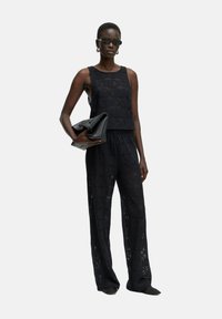 Zwarte gehaakte tweedelige set met een mouwloze top en wijde broek, met een geometrisch patroon en gecombineerd met een zwarte clutch.