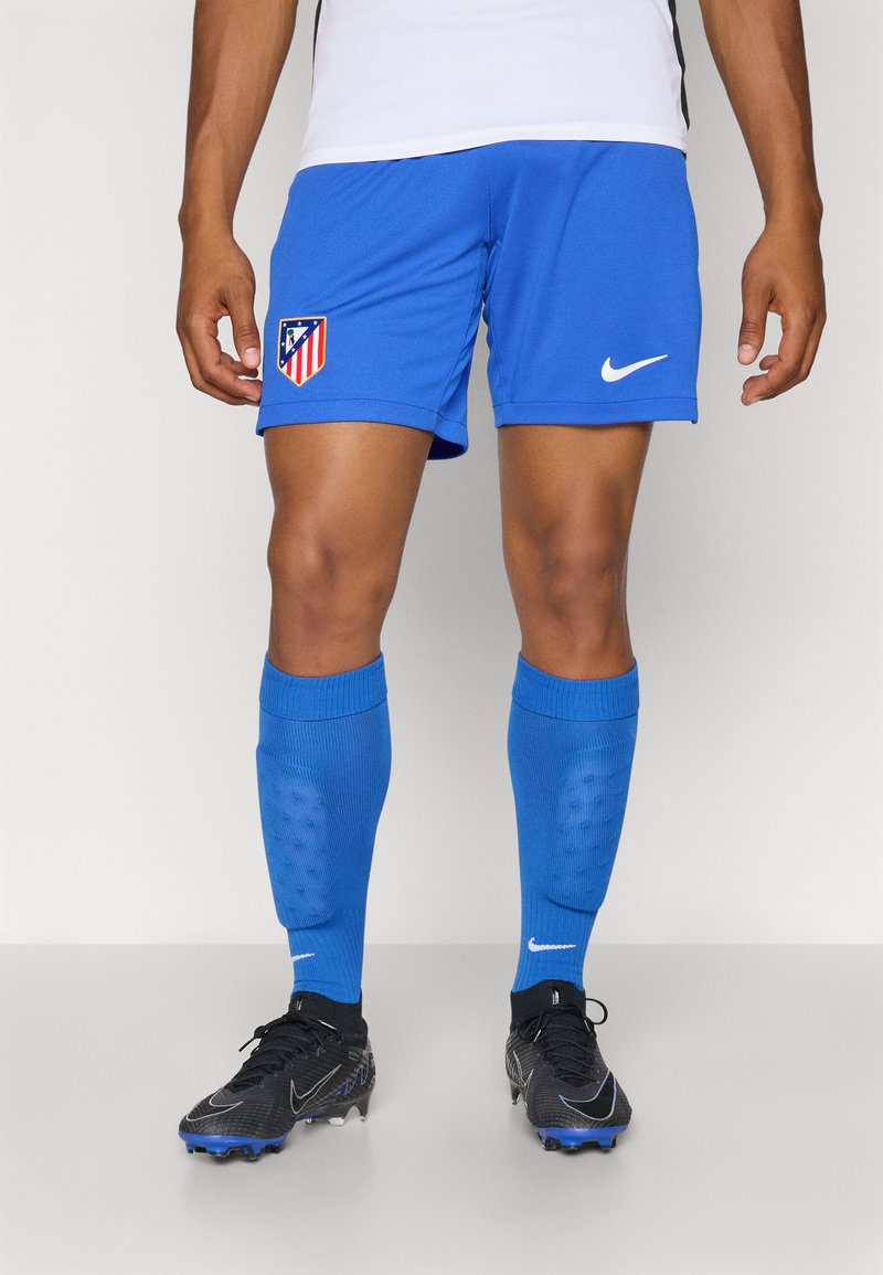 Blå fodboldshorts med Atlético Madrid-logo, parret med matchende blå sokker og sorte strukturerede støvler med en hvid Nike-swoosh.