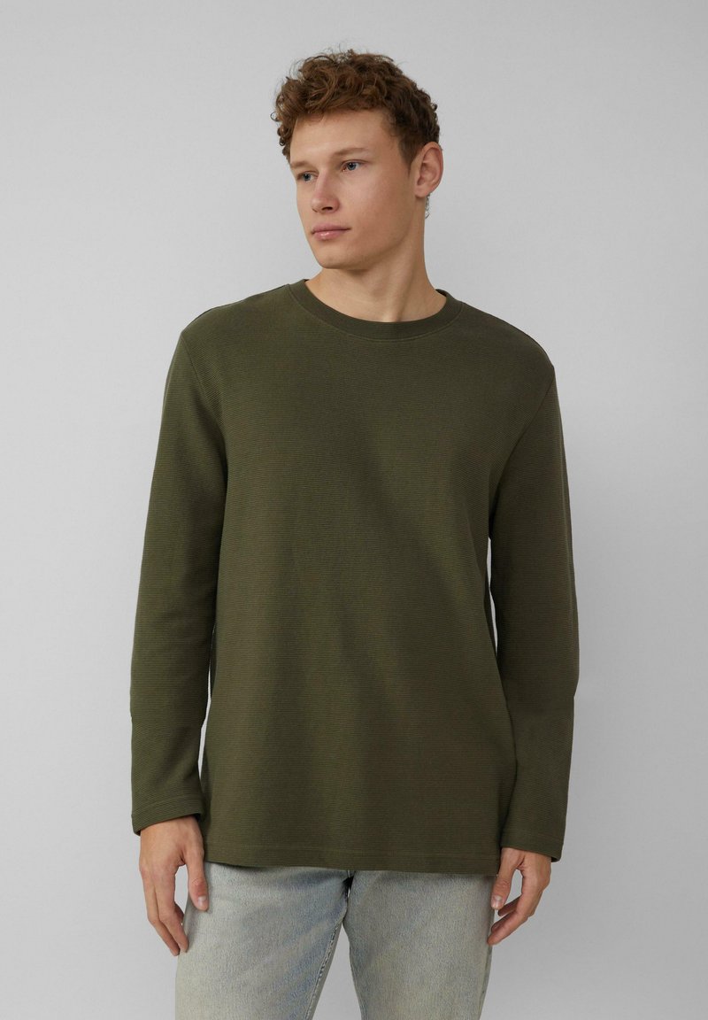 Olijfgroene langemouwen shirt van een gestructureerde stof, met een ronde hals en rechte zoom, gedragen met lichtblauwe jeans.