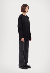Črna oversize majica s dolgimi rokavi, ki ima majhen rumen dizajn. V kombinaciji s temno sivo denim hlačami in črnimi platform čevlji.