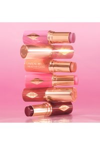 Sechs zylindrische Lippenstifthülsen in verschiedenen Rosa-, Korallen- und Mauvetönen, mit goldenen Akzenten und einem glänzenden Finish, gestapelt vor einem rosa Hintergrund.