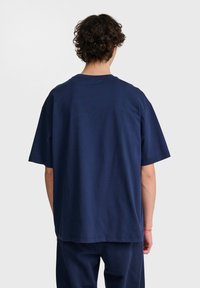 Marinblå bomullströja med avslappnad passform, korta ärmar och rundad halsringning, med en slät textur och minimala sömmar på baksidan.