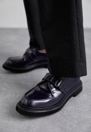 Pantofi din piele încălțată purpurie cu vârful rotund, o curea cu cataramă și o talpă groasă din cauciuc negru cu caneluri. Purtați cu pantaloni negri.
