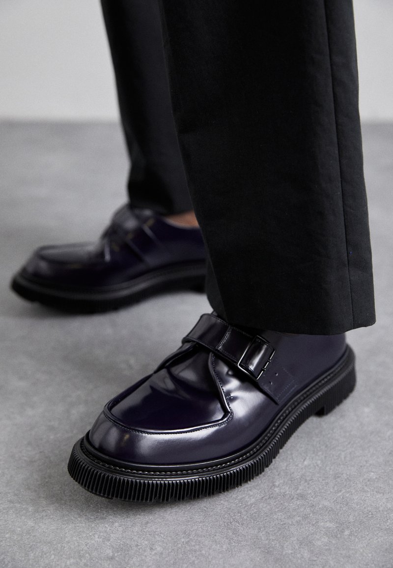 Pantofi din piele încălțată purpurie cu vârful rotund, o curea cu cataramă și o talpă groasă din cauciuc negru cu caneluri. Purtați cu pantaloni negri.