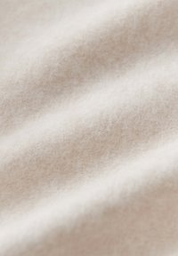 Helles beiges Gewebe mit einer weichen, strukturierten Oberfläche und subtilen Farbvariationen, das sanfte Wellen und Falten aufweist.