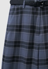Grau karierte Hose mit glatter Textur, ausgestattet mit schwarzen und weißen Akzenten. Inklusive einem schwarzen Ledergürtel und Seitentaschen.