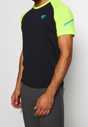 Mann trägt schwarzes und neongelbes athletisches Kurzarmshirt mit blauem Logo auf der Brust und "DYNAFIT" Schriftzug auf dem rechten Ärmel.
