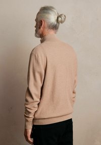 Beżowy sweter z dzianiny o wysokim kołnierzu, ściągaczami na mankietach i u dołu; zestawiony z czarnymi spodniami. Tekstura wydaje się miękka z delikatnym wzorem.