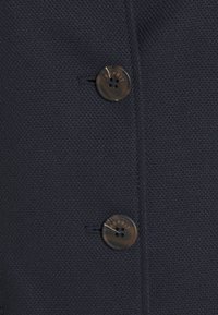 Marinblått strukturerat tyg med två knappar. Knapparna är cirkulära, tillverkade av plastmaterial med en subtil marmorering, präglade med "ESPRIT."