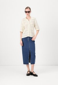 Kremfarget strikket cardigan med korte ermer, kombinert med et høyt liv denimskjørt med et frontslitt. Svart sko og solbriller.