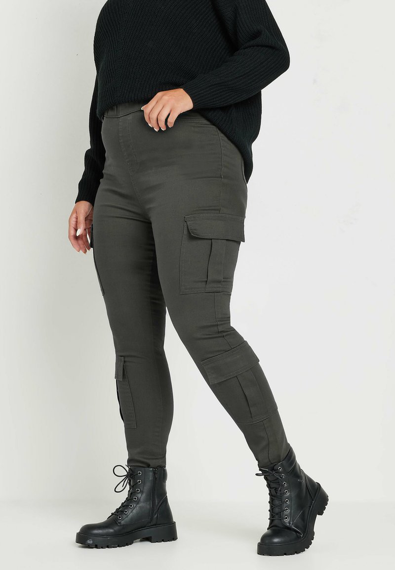 Pantalones cargo caqui con múltiples bolsillos, un ajuste slim y una cintura de altura media, combinados con botas de combate negras con cordones. Suéter negro de punto texturizado.