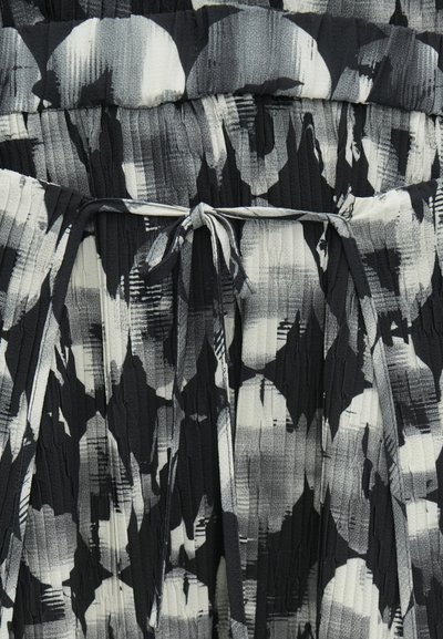 Μαύρο και λευκό πλισέ φόρεμα με αφηρημένο σχέδιο, με υφασμάτινη κορδέλα στη μέση και υφασμάτινες λεπτομέρειες στην επιφάνεια.