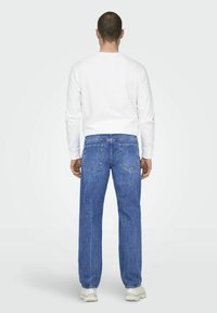 Jeans de mezclilla azul con corte recto, diseño de cinco bolsillos y detalles de costura sutil; combinados con una camisa de manga larga blanca.