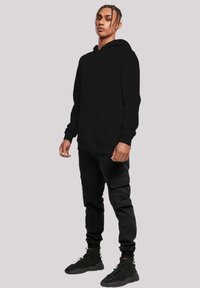 Schwarzer Hoodie mit Kängurutasche, geripptem Saum und Bündchen, kombiniert mit schwarzen Cargo-Hosen und High-Top-Sneakern. Das Material erscheint weich.