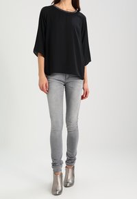 Schwarze, locker sitzende Bluse mit einem runden Halsausschnitt und kurzen Ärmeln, kombiniert mit grauen Skinny-Jeans und metallischen Chelsea-Boots.