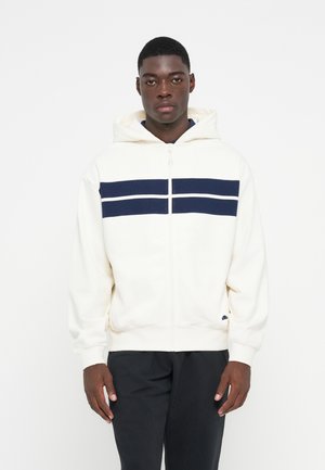 Hvid zip-up hættetrøje med et marineblåt stribet design over brystet, stor hætte, ribbede manchetter og lomme foran.