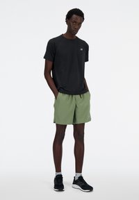Black athletic t-shirt and light green shorts. Shirt has a subtle logo; shorts are knee-length with an elastic waistband and pockets.
