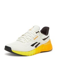 Białe buty sportowe z czarnymi akcentami i pomarańczowym logo. Charakteryzują się siateczkową cholewką, teksturowaną podeszwą i jasnofioletowym obcasem. Lekka konstrukcja.
