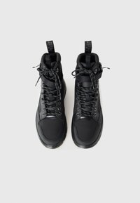 Paire de baskets montantes noires en tissu texturé, lacets sur le devant, sangles à la cheville et languettes sur fond gris clair.