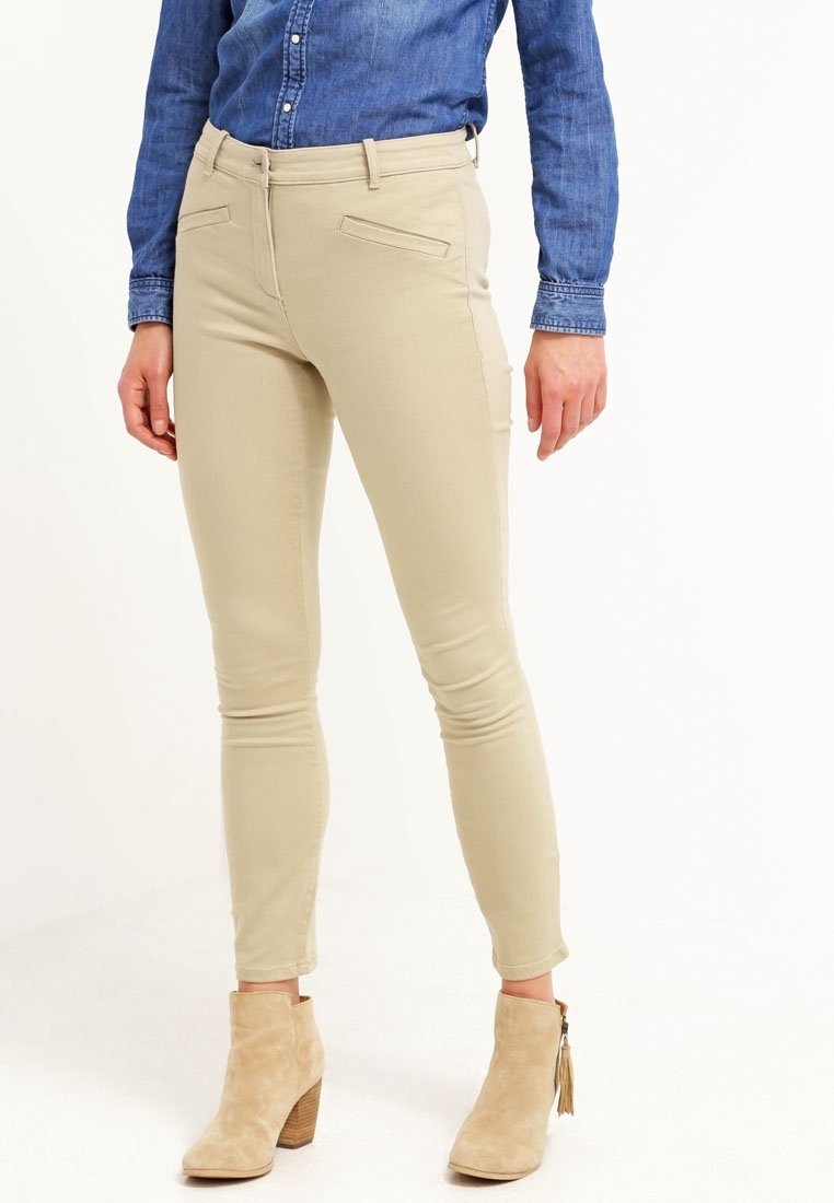 Pantalons skinny beige avec une texture lisse, poches avant et taille mi-haute, associés à des bottes de cheville beige clair avec un talon en bois.