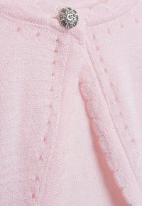Helles rosa gestricktes Sweatshirt mit glitzernden Fäden, das mit einem gewellten Saum und einem dekorativen silbernen blütenförmigen Knopf ausgestattet ist.