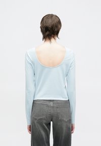 Ανοιχτό μπλε μπλουζάκι με μακριά μανίκια και ανοιχτή πλάτη σε σχήμα scoop, κατασκευασμένο από μαλακό ύφασμα. Συνδυάζεται με γκρι τζιν παντελόνι με τσέπες και υφή.