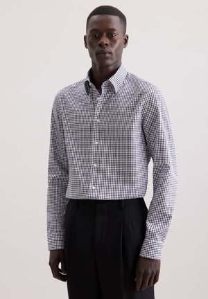Camicia a maniche lunghe in tessuto di cotone, con una stampa a scacchi bianca e nera. Presenta un colletto ed è abbinata a pantaloni neri.