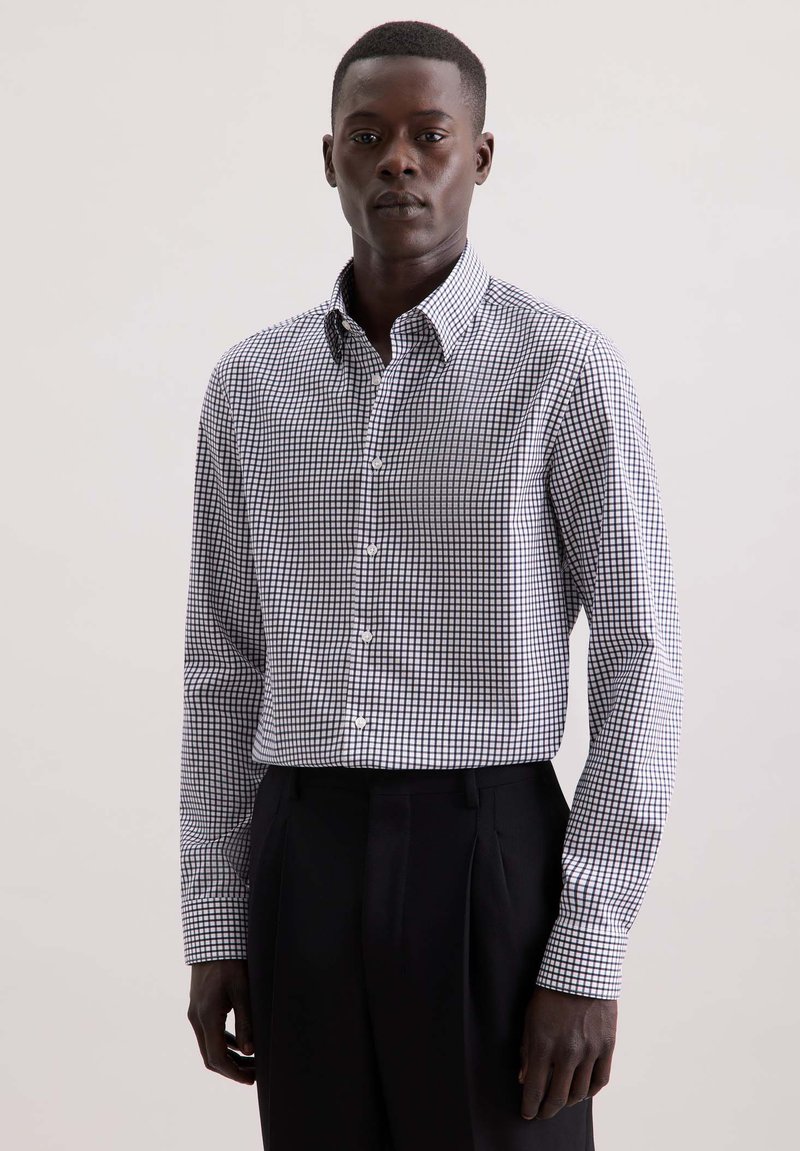 Overhemd met knoopsluiting in een zwart-wit geruit patroon, gemaakt van katoen. Beschikt over lange mouwen en een kraag, gedragen met zwarte broek.