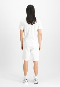Tricou alb din bumbac, cu guler rotund și mâneci scurte, purtat cu șorturi albe până la genunchi. Încălțămintea are detalii alb și gri.