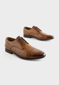 Zapatos de vestir de cuero marrón con punta afilada, diseño de cordones y sutiles detalles de costura. Textura suave y tacón bajo.
