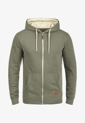 Alyvuogių žalios zip-uotos džinsinės striukės, pagamintos iš minkštos medžiagos, su smėlio spalvos vidumi, raišteliais, priekinėmis kišenėmis ir odiniu logotipo ženklu.