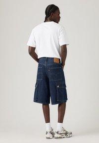 Shorts cargo din denim de culoare albastru închis, cu multiple buzunare, din țesătură de bumbac, tăietură dreptă. Asortați cu un tricou alb simplu și adidași argintii.