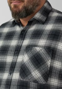 Camicia in flanella a quadri bianca e nera con design a bottoni, taschino sul petto e tessuto testurizzato. Presenta bottoni scuri e logo sulla tasca.