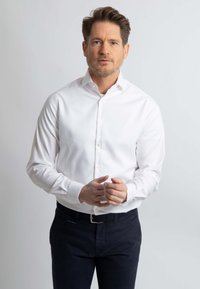 Witte button-up blouse gemaakt van gladde stof, met lange mouwen, een smalle kraag en een getailleerd ontwerp, gecombineerd met donkere trousers.