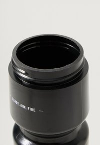 Bouteille cylindrique noire avec une surface texturée. Le dessus présente une large ouverture et un texte blanc indiquant "PRÊT, VISEZ, TIREZ." Fini lisse.