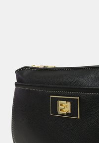 Borsa a tracolla in pelle nera con finitura testurizzata, dettagli in metallo dorato, chiusura a zip e cuciture a contrasto lungo i bordi. Design compatto e strutturato.