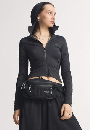Zwarte zip-up top met lange mouwen en een capuchon, met een gatherede textuur, gecombineerd met een zwarte heuptas met ritsen en verstelbare banden.