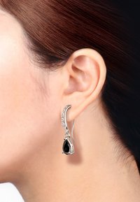 Sølvdråbeøreringe med en sort gemstone vedhæng og et buet design med små klare accenter langs den øverste kant.