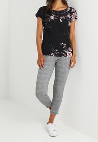 Top negro con estampado floral, mangas cortas; pantalones de cuadros grises, ajuste tapered; zapatillas blancas. Diseño simple con una mezcla de patrones y colores.